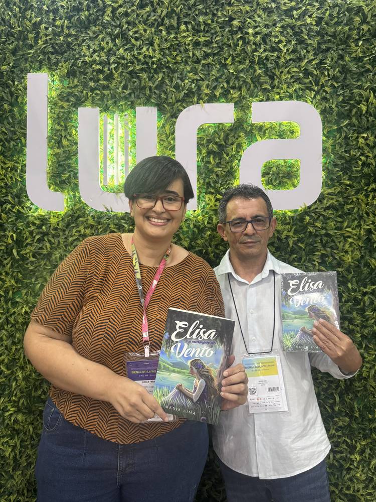 Régis Lima de blazer ao lado de uma leitora, diante do painel da editora