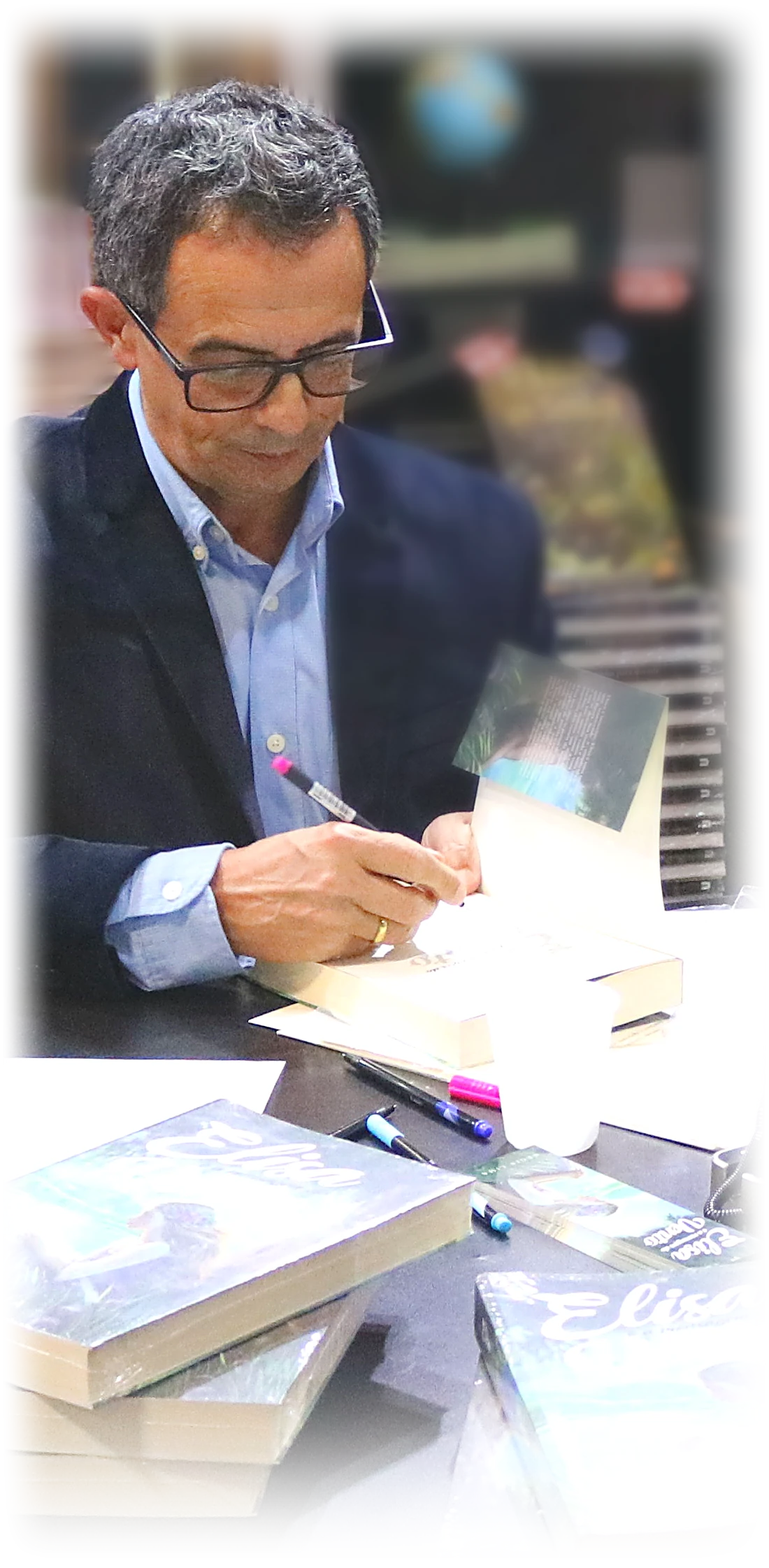 Régis Lima assinando uma dedicatória à caneta na folha de rosto de um exemplar, na Bienal Internacional do Livro de São Paulo, 2024
